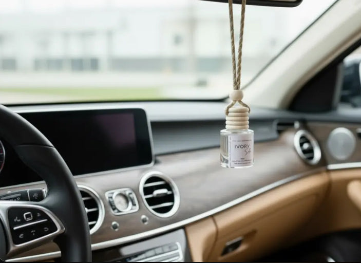 A clear glass car air freshener bottle with a beige rope hanging suspension, displayed inside a luxury car's dashboard.